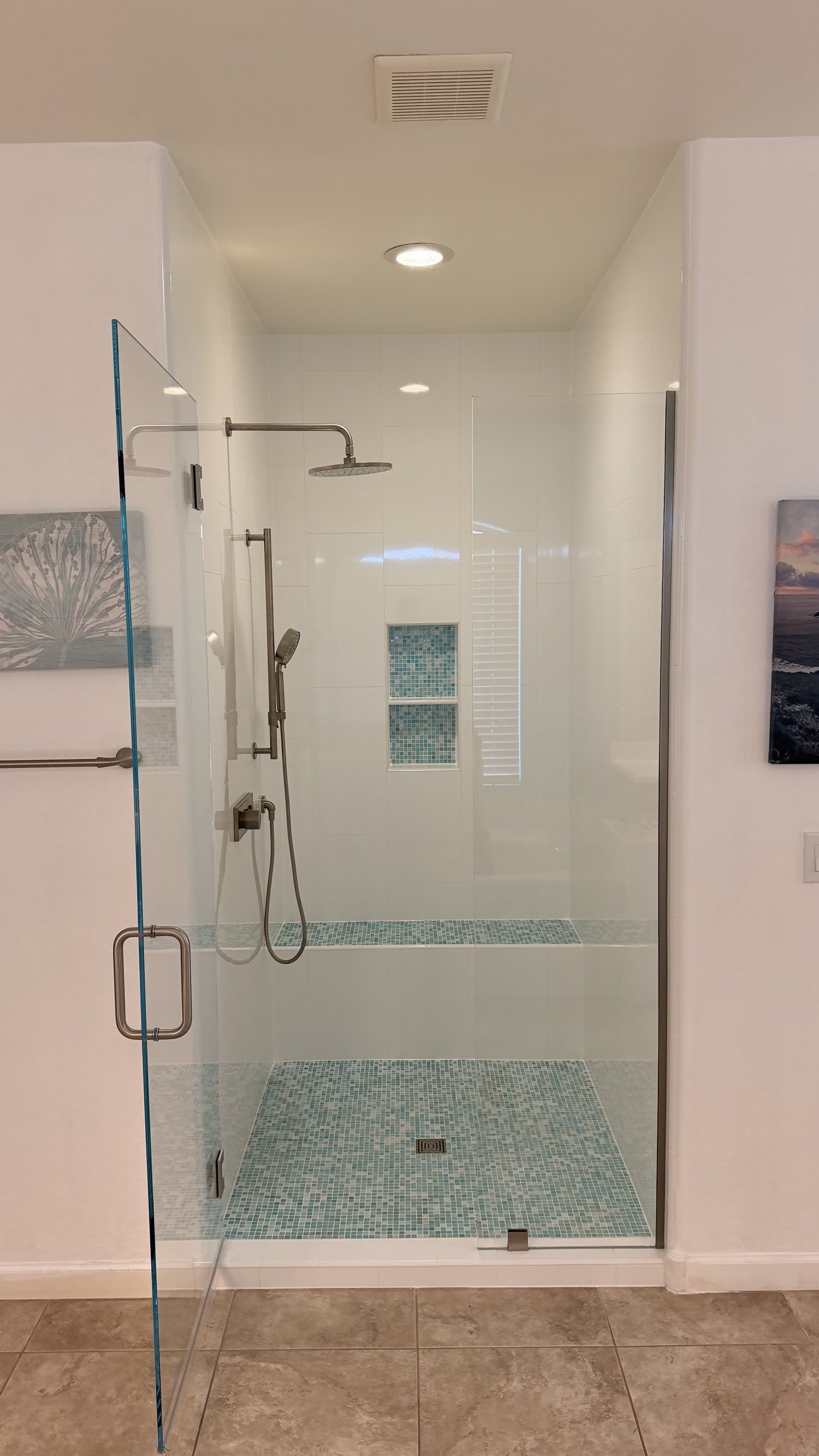 White tile shower with an aqua mosaic floor, bench, and niche