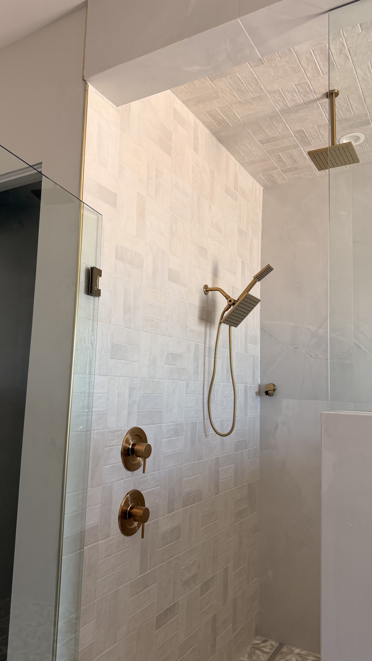 Herringbone wall tile with brushed-gold fixtures and a ceiling rain head