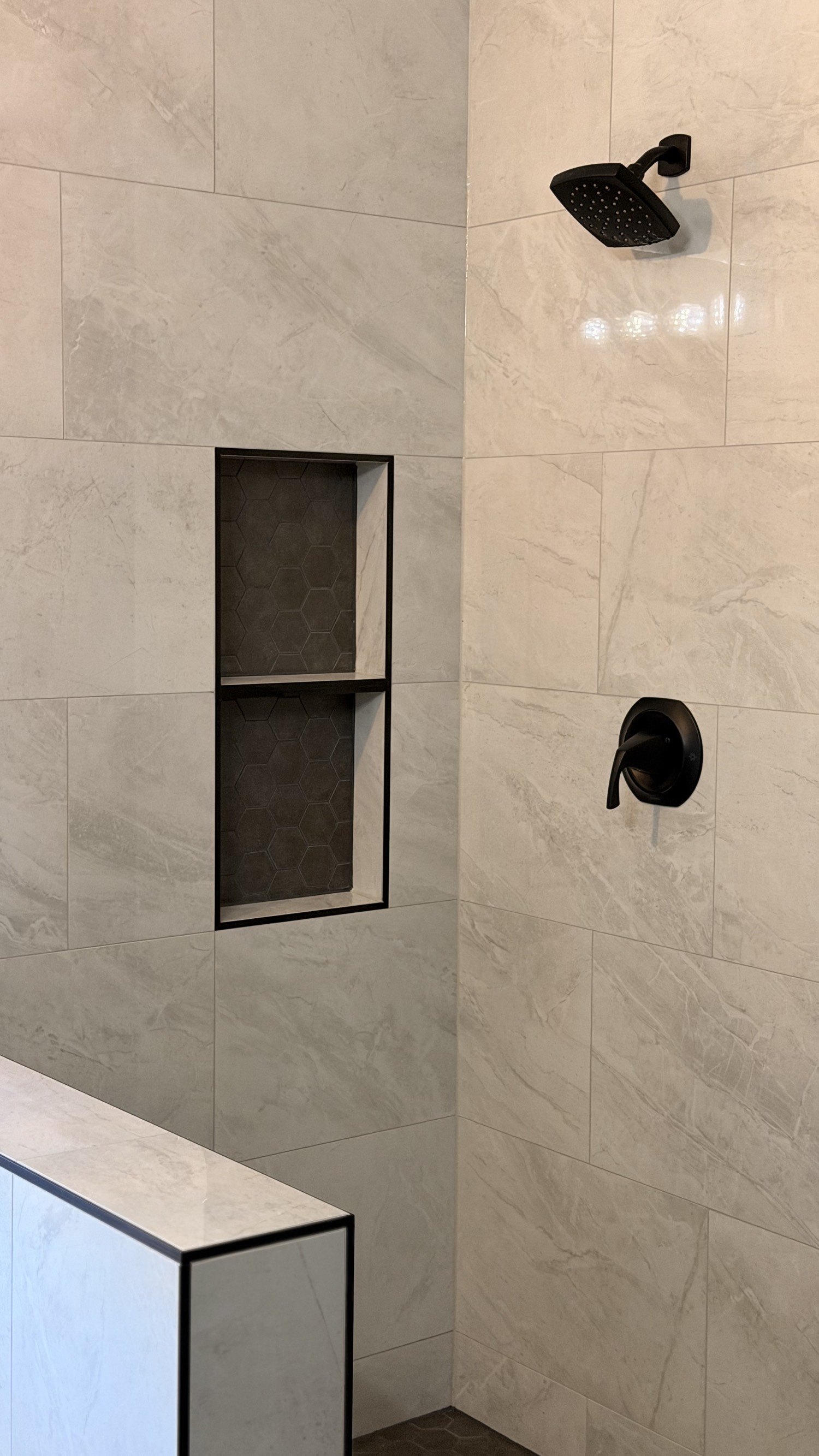 Marble shower wall with a black-trimmed niche and matte black fixtures